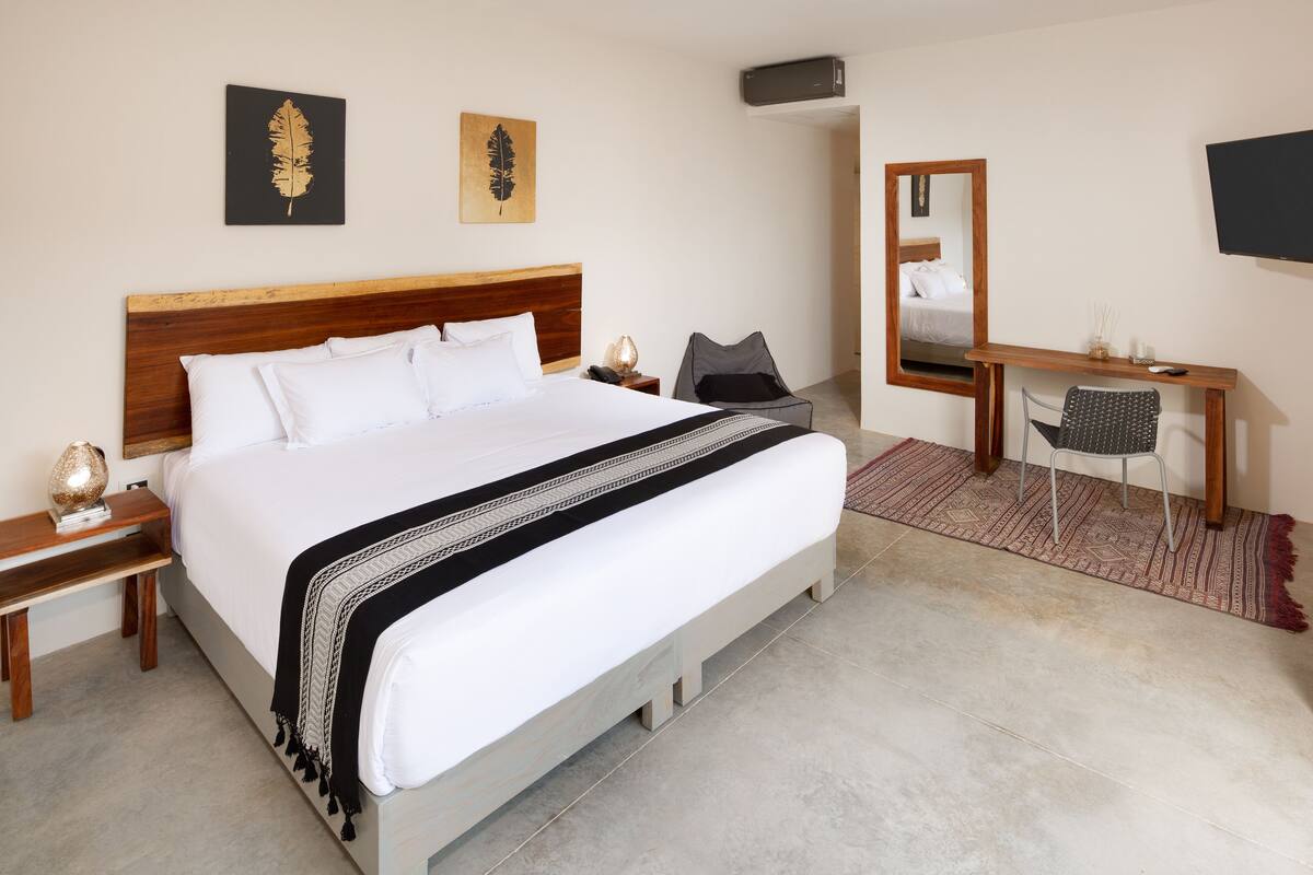 A hotel room with a large bed, a desk, a chair, a mirror, and artwork on the walls.