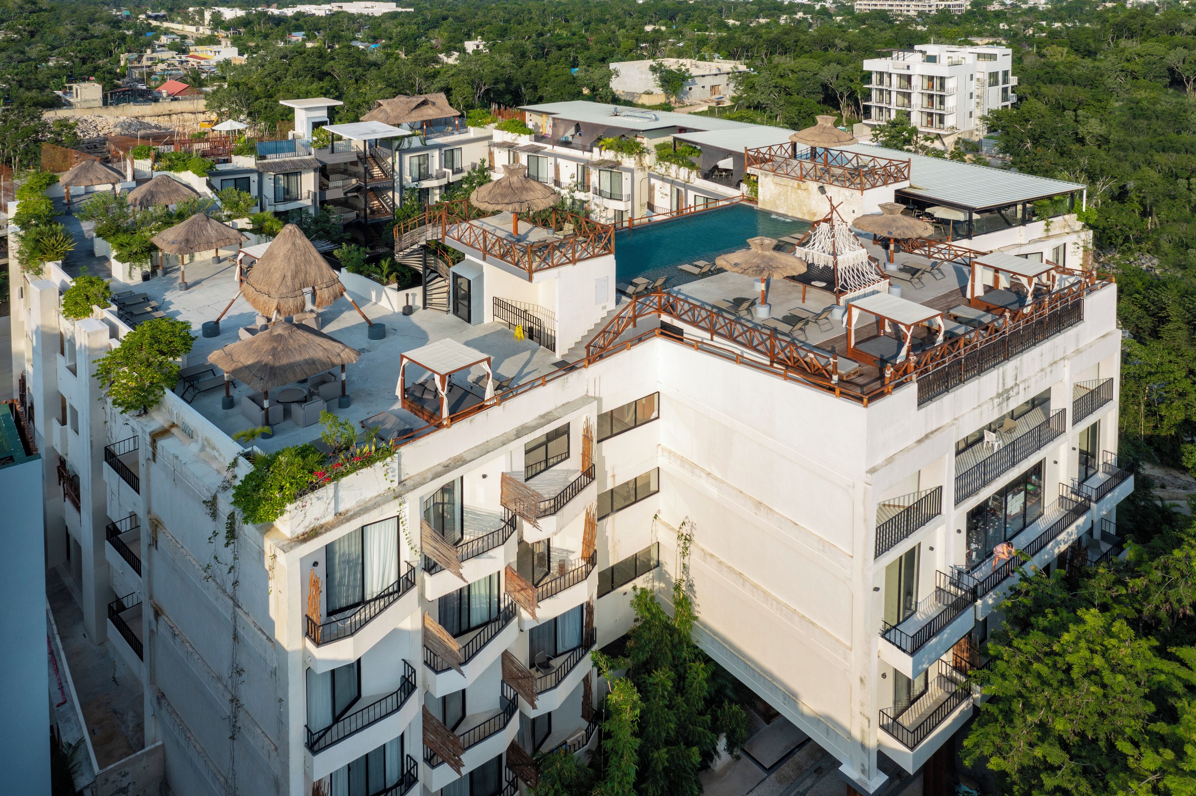 A multi-story hotel with a rooftop pool, outdoor seating, and a lush surrounding environment.
