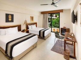 Habitación de hotel con dos camas, televisión, escritorio y balcón con vistas a zonas verdes.