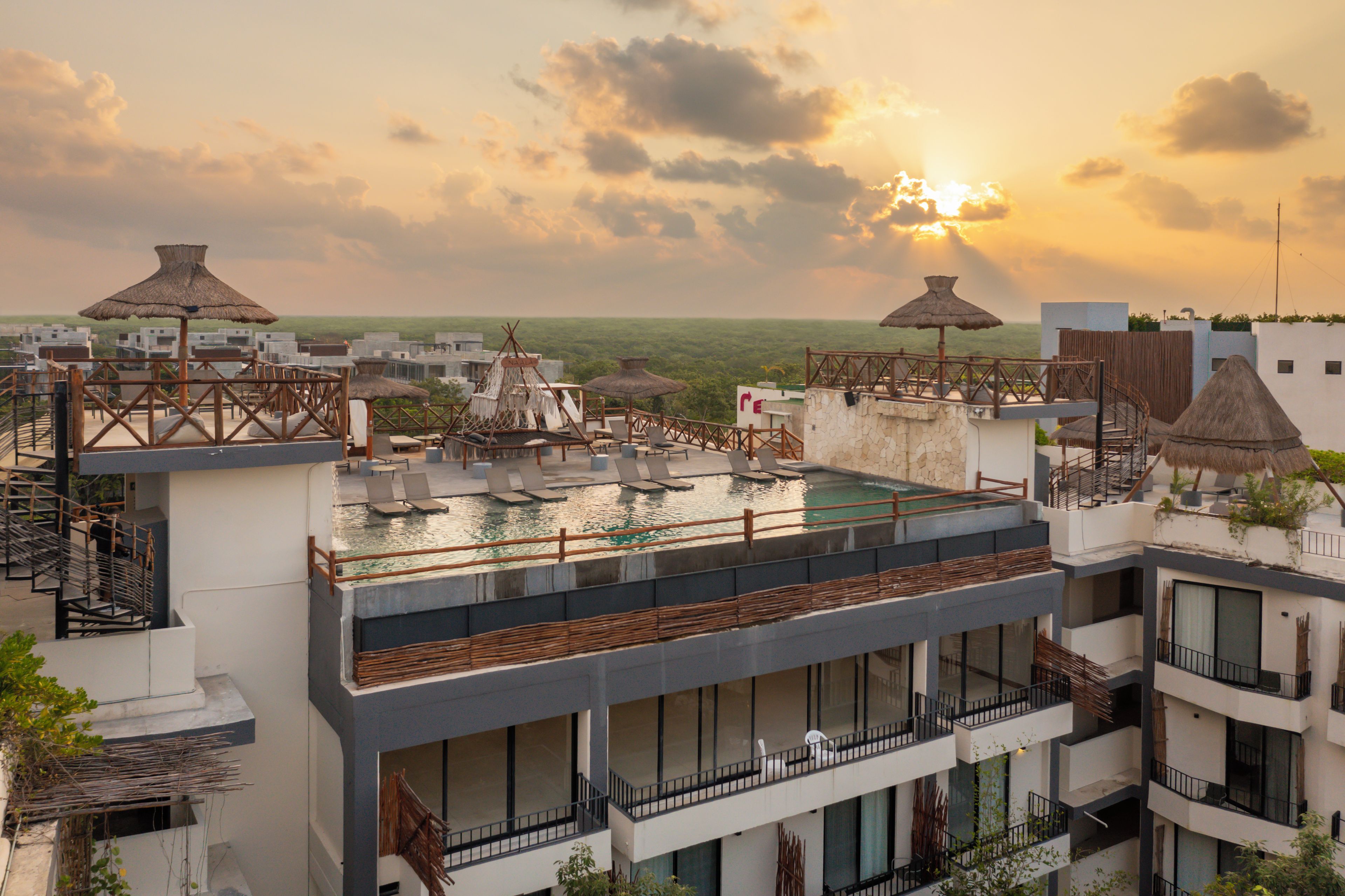 A rooftop pool area with lounge chairs and thatched umbrellas, surrounded by modern buildings.