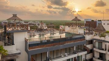 A rooftop pool area with lounge chairs and thatched umbrellas, surrounded by modern buildings.