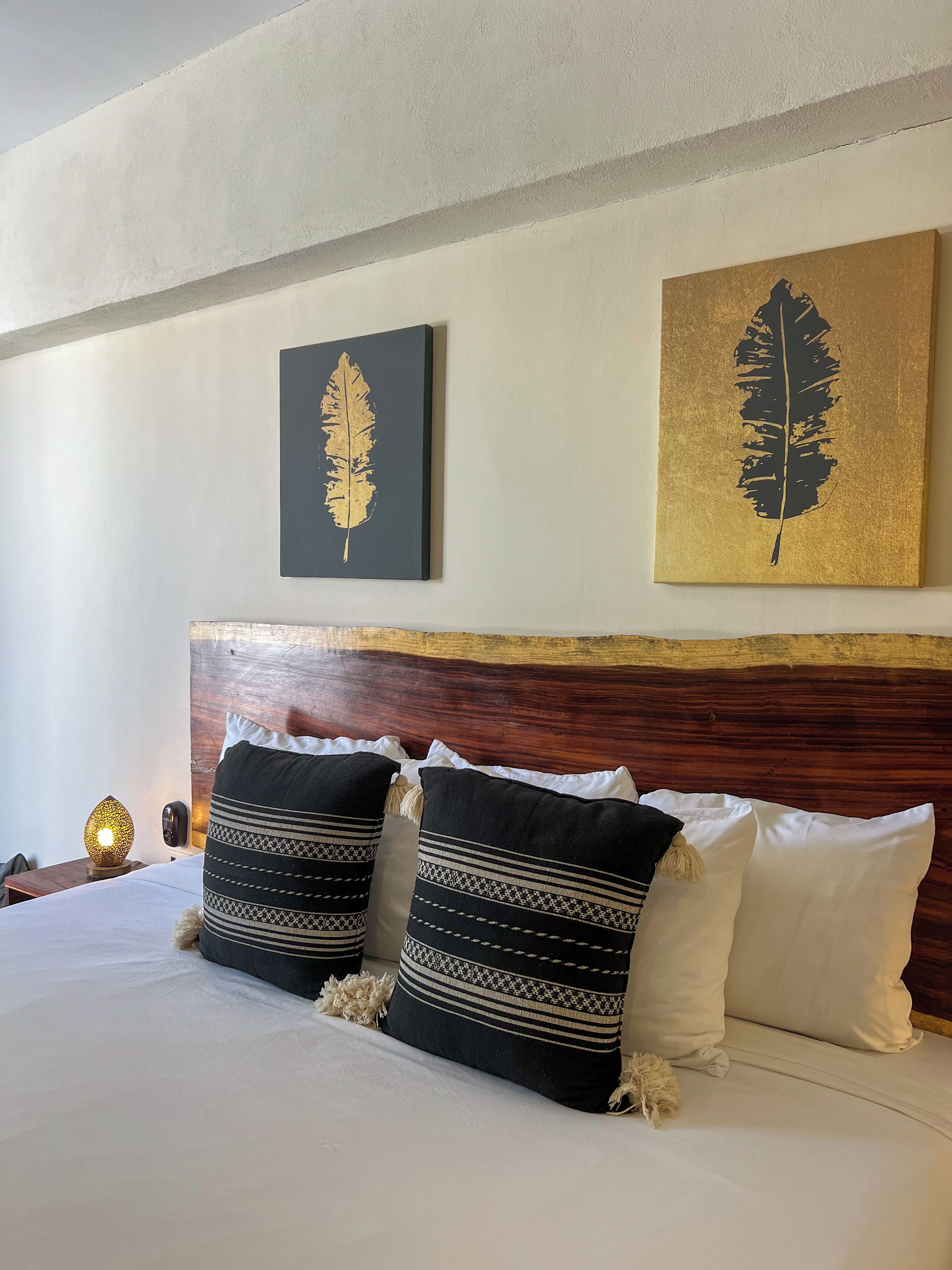 A hotel room with a wooden headboard, a bed with white and black striped pillows, and two wall art pieces above the bed.