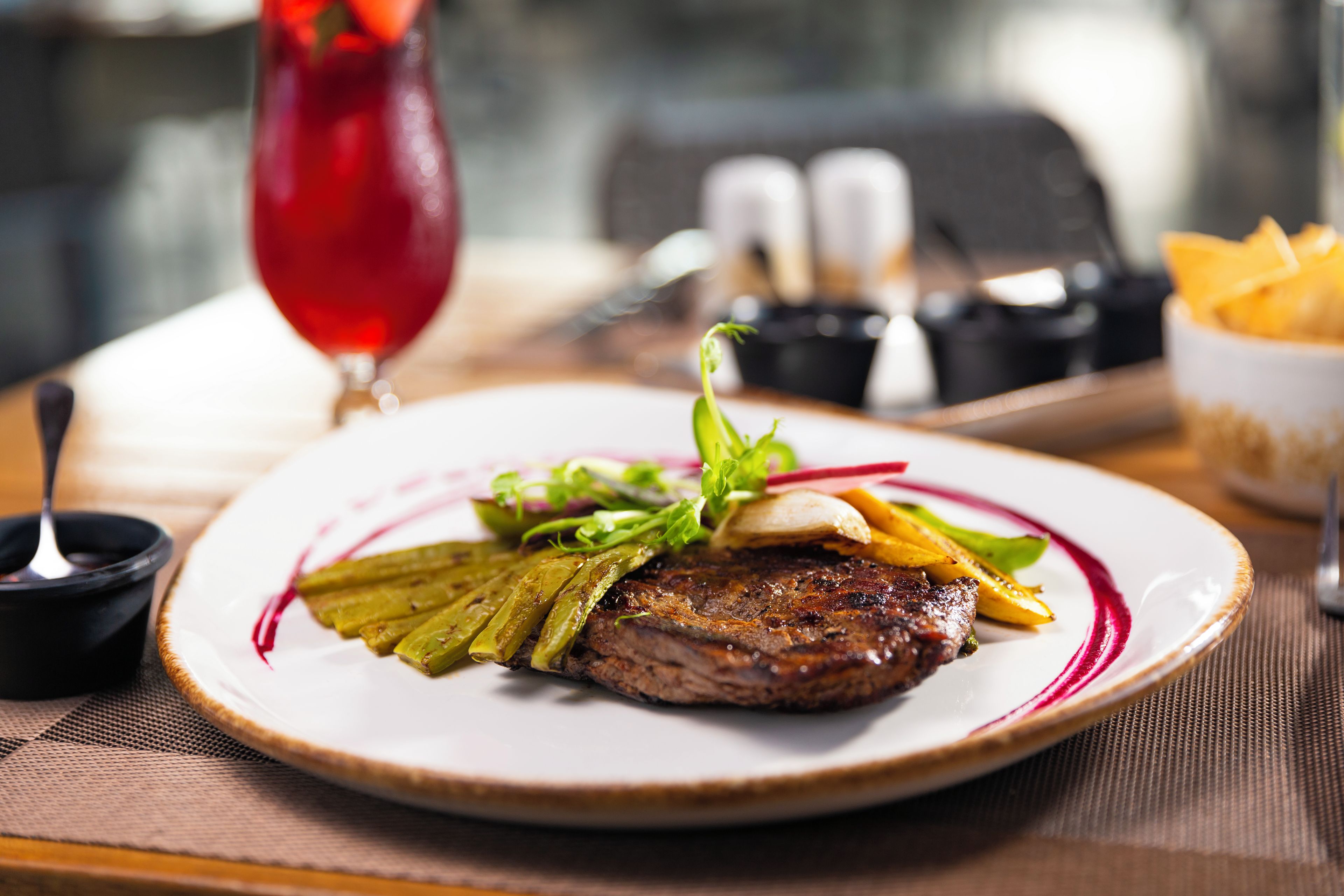 Une assiette contenant un steak, des légumes et une sauce rouge, posée sur une table.