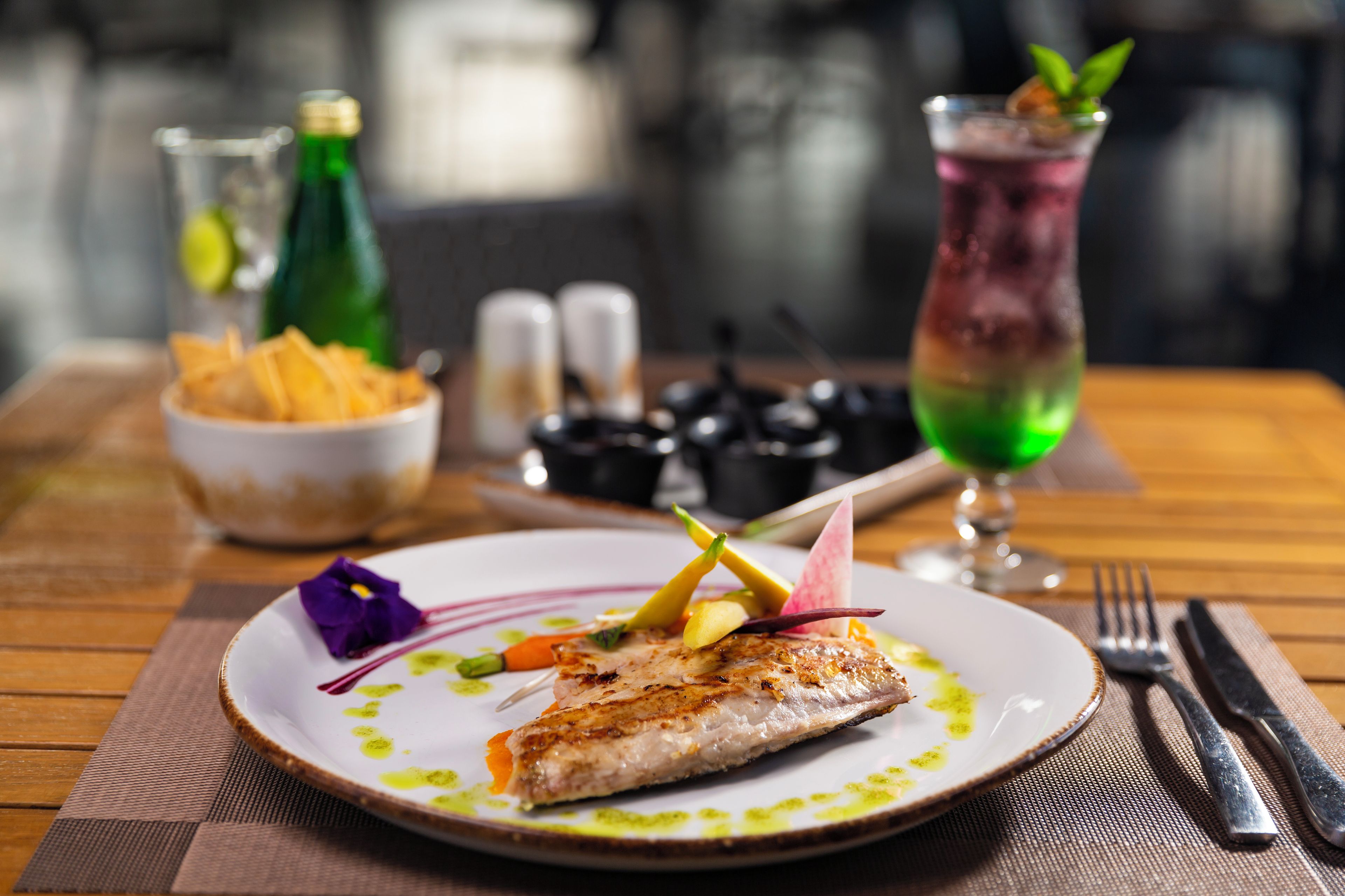 Una mesa de comedor con un plato de comida, una botella y un vaso de bebida.