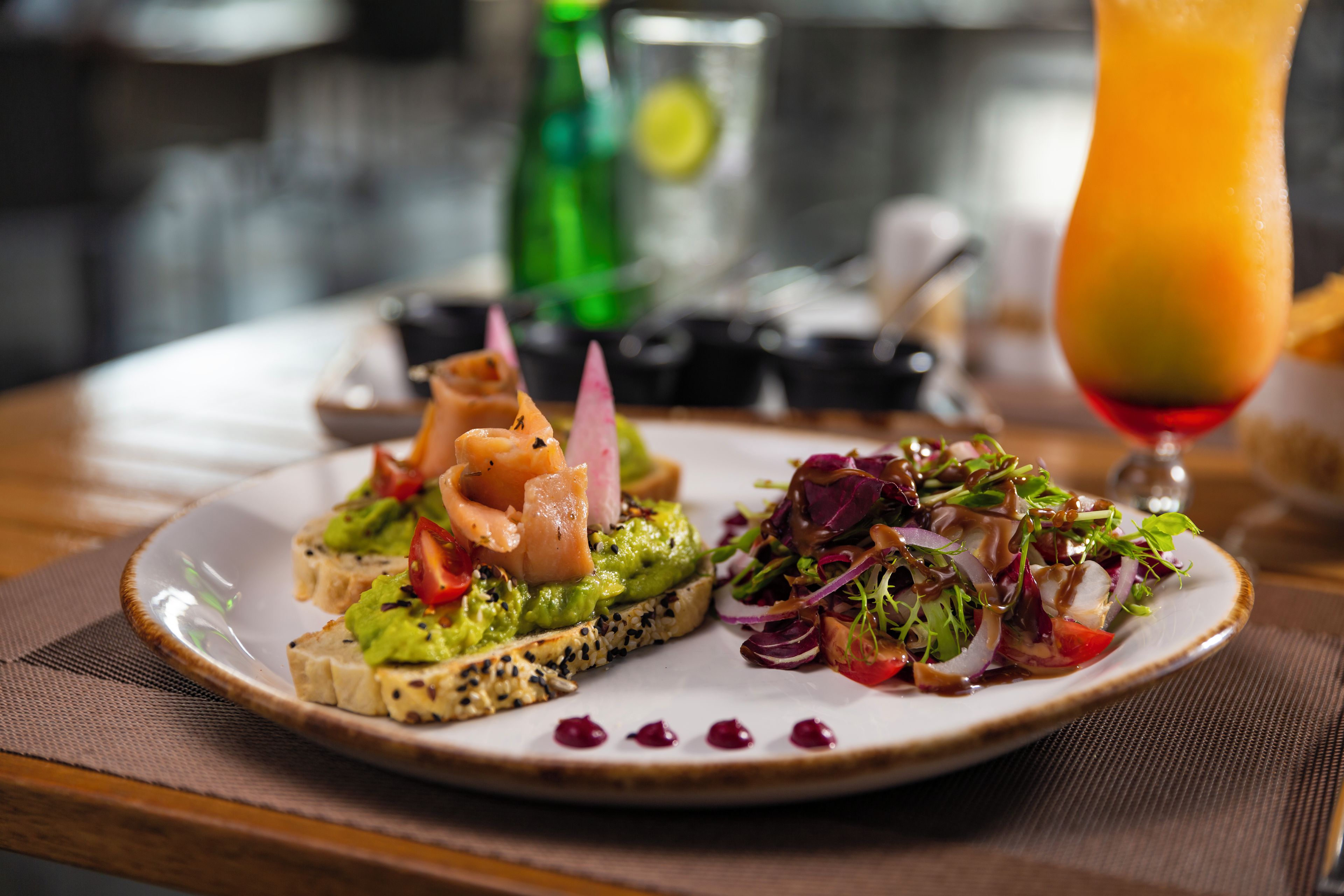 A plate with two types of food, one with avocado and salmon, the other with a salad, on a table with a glass of orange juice.
