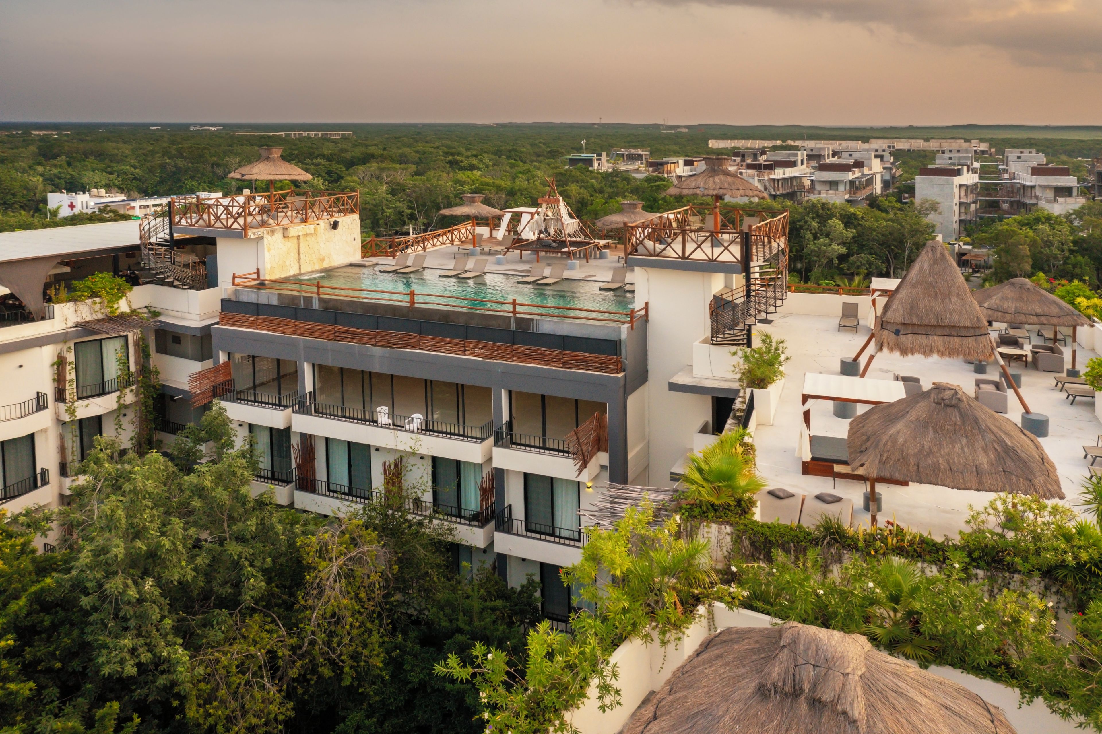 A resort with multiple buildings, including a rooftop pool area with lounge chairs and a thatched-roof structure.