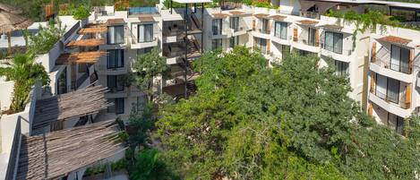 A modern residential complex with multiple balconies, a rooftop garden, and a view of the surrounding landscape.