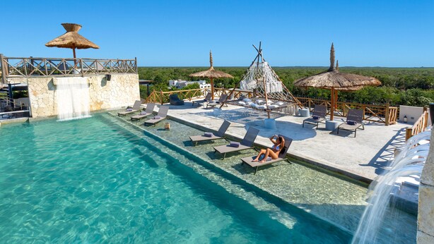 A clear pool with lounge chairs and umbrellas, surrounded by a stone deck and a waterfall feature. - Sunday Hotel Naala Tulum (Tulum)