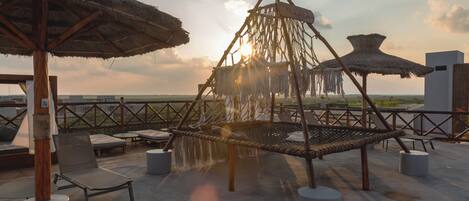 A rooftop lounge with thatched umbrellas, lounge chairs, and a wooden structure.