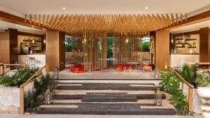 A modern hotel lobby with a central staircase, wooden railings, and a bar area with shelves of bottles. - Sunday Hotel Naala Tulum (Tulum)
