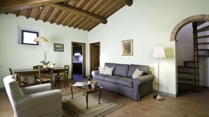 A cozy living room with a sofa, armchair, dining table, and a staircase leading to an upper level. - Colombaio Apartment (Pietraviva)