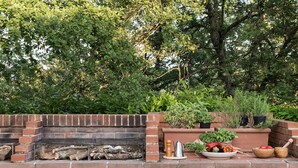 A brick barbecue grill with a wooden bench, surrounded by potted plants and a variety of vegetables. - Colombaio Apartment (Pietraviva)