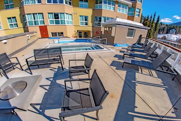 A rooftop pool area with lounge chairs, a hot tub, and a lifebuoy.