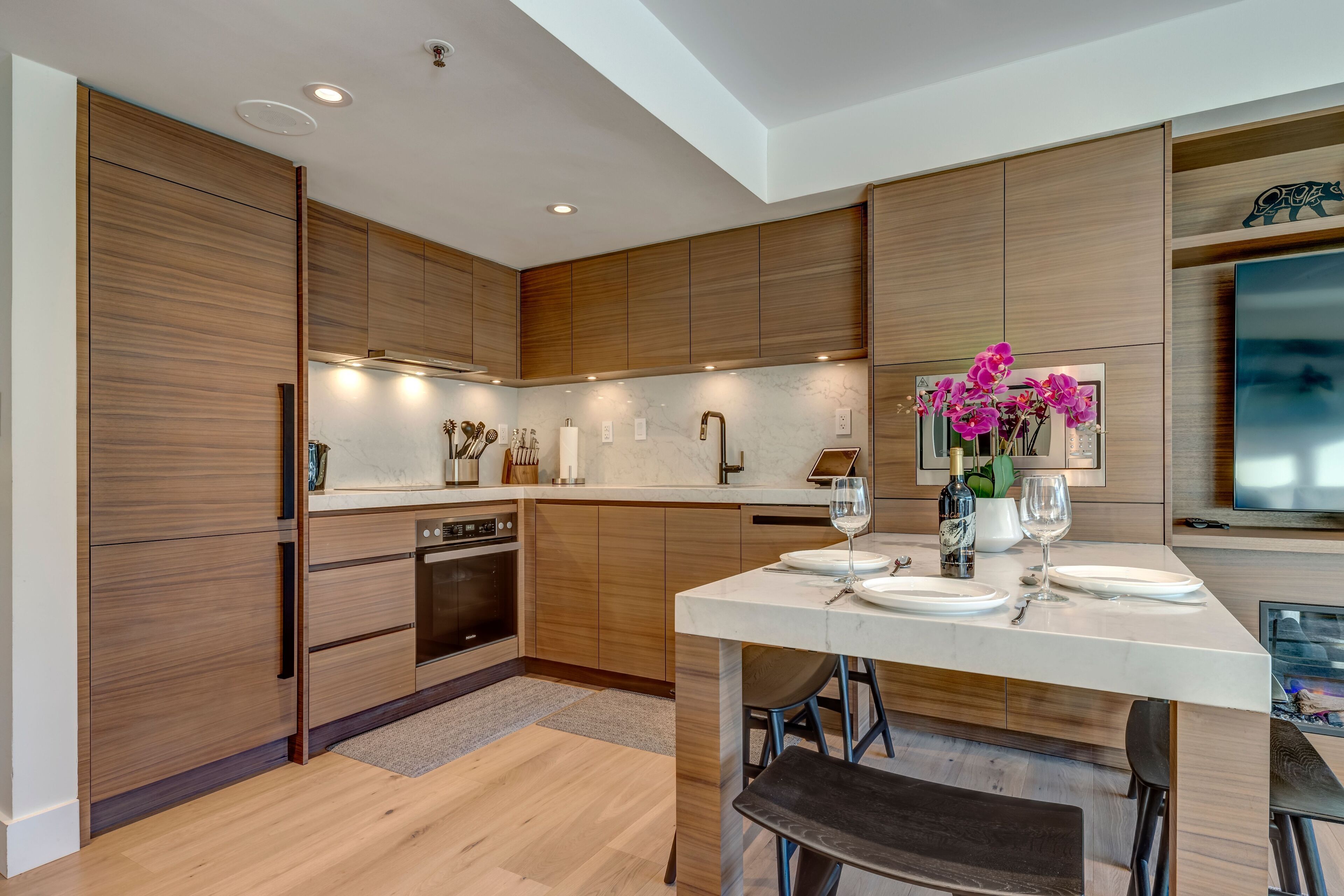 A modern kitchen with wooden cabinets, a central island, and a dining area with bar stools.