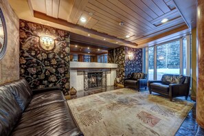 A cozy living room with a fireplace, leather sofas, and large windows offering a view of the outdoors.