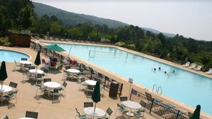 A pool area with lounge chairs and tables, surrounded by a fence, with a view of trees and hills in the background. -  lake front, dock, hot tub, Clemson, 7 bedrooms, 7 baths, kayaks, waterfalls ,  (Westminster)