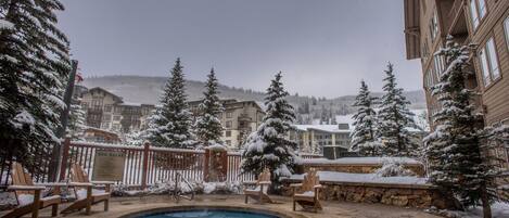 A pool area with a hot tub, wooden chairs, and a stone deck.