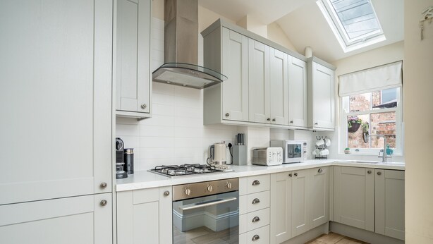 Een moderne keuken met witte kasten, een gasfornuis, een oven en een dakraam.