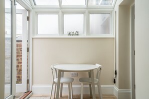 A room with a white table and two chairs, a window with frosted glass panes, and a view of a brick wall outside.