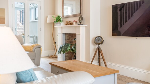 A living room with a sofa, a wooden coffee table, a fireplace, a mounted clock, and a framed picture on the wall.