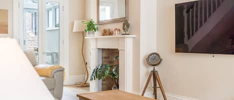 Una sala de estar con un sofá, una mesa de centro de madera, una chimenea, un reloj montado y un cuadro en la pared.