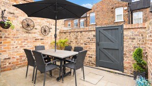 A patio with a table and chairs, a black umbrella, and a stone wall.