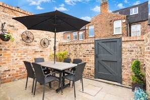 Un patio con una mesa, sillas, un paraguas negro y un muro de piedra.