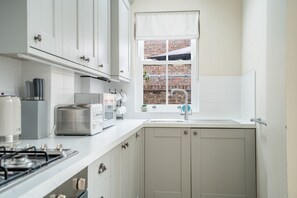 A kitchen with white cabinets, a window with a view of a brick wall, a sink, and a stove.