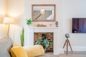 A living room with a fireplace, a mounted mirror, a lamp, and a television on the wall.