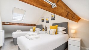 A modern bedroom with a sloped ceiling, a skylight, a bed with white bedding, a bedside table with a lamp, and artwork on the wall.