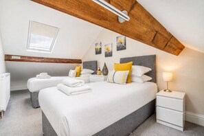 Un dormitorio moderno con techo inclinado, un tragaluz, una cama con ropa de cama blanca, una mesita de noche con lámpara y una obra de arte en la pared.