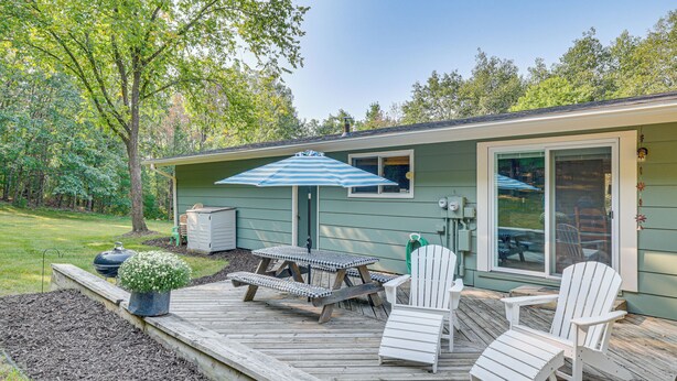 Un patio con tavolo da picnic, due poltrone Adirondack e un ombrellone a righe blu.