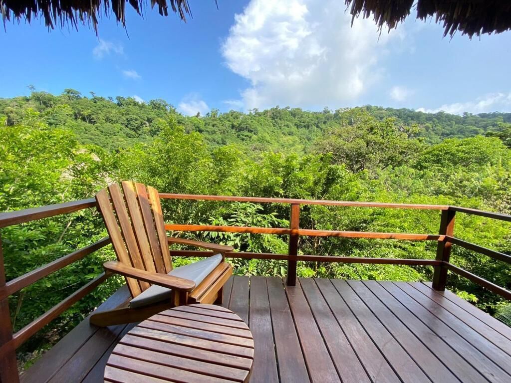 A wooden deck with a bench and a table overlooking a lush green forest.