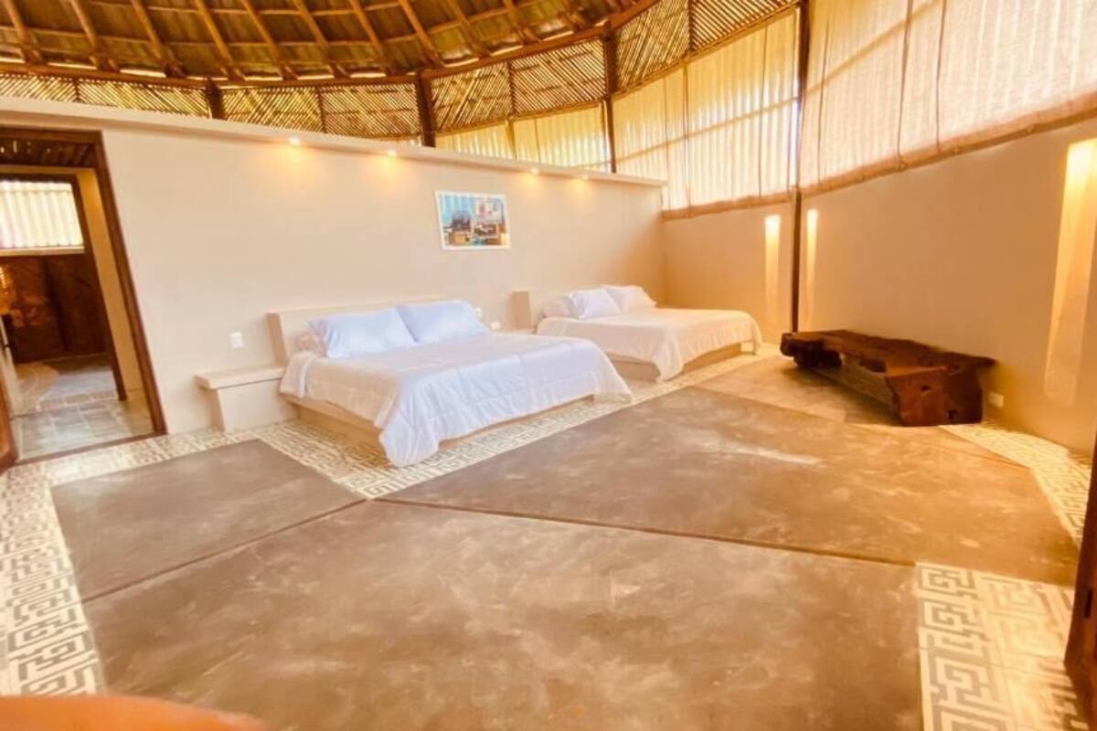 A room with two beds, a wooden bench, and a thatched ceiling.