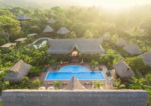 A resort with a central swimming pool surrounded by thatched-roof structures and lush greenery. - Senda Koguiwa (Santa Marta)