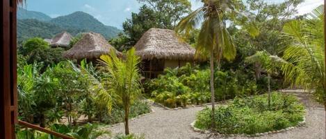 A tropical garden with thatched-roof huts, palm trees, and lush greenery.