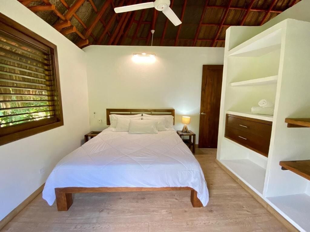 A bedroom with a bed, a ceiling fan, a nightstand, a lamp, and built-in shelving.