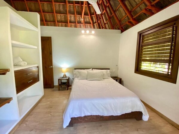 A bedroom with a bed, bedside tables, a nightstand, a lamp, a wardrobe, and a window with blinds. - Senda Koguiwa (Santa Marta)