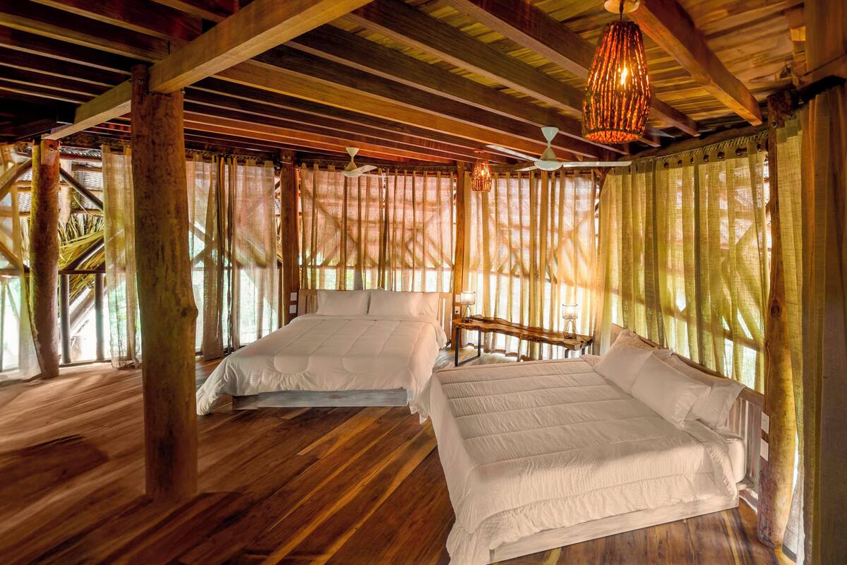 A room with two beds, wooden floors, and a sloped ceiling with exposed beams.