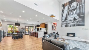 A spacious living area with a kitchen, dining area, and a large artwork of a pier. - 4BR Resort Near Beach/Disney; Pool is +$149 /night (Huntington Beach)