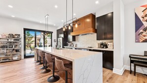A modern kitchen with a marble island, wooden cabinets, and a piano. - 4BR Resort Near Beach/Disney; Pool is +$149 /night (Huntington Beach)