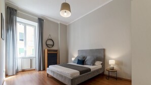 A bedroom with a bed, a bedside lamp, a window with curtains, and a radiator.