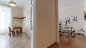 An open-plan living area with a dining table and chairs, a kitchen area with a shelf, and a hallway leading to another room.