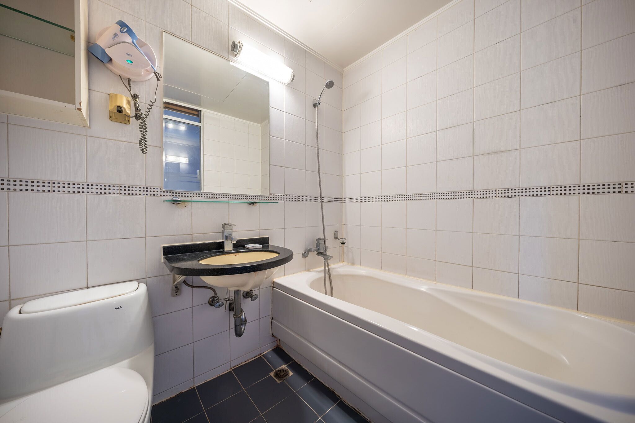 Ein Badezimmer mit einer weißen Badewanne, einem Waschbecken mit schwarzer Arbeitsplatte und einer Toilette.