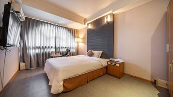 Habitación de hotel con una cama grande, un escritorio, una silla, una lámpara y un televisor de pantalla plana.