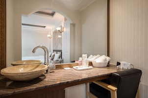 Un baño con un lavabo de mármol grande, un espejo y una zona de tocador con artículos de aseo.