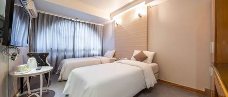 A hotel room with two beds, a small table with a kettle and a cup, a TV, and a window with curtains.