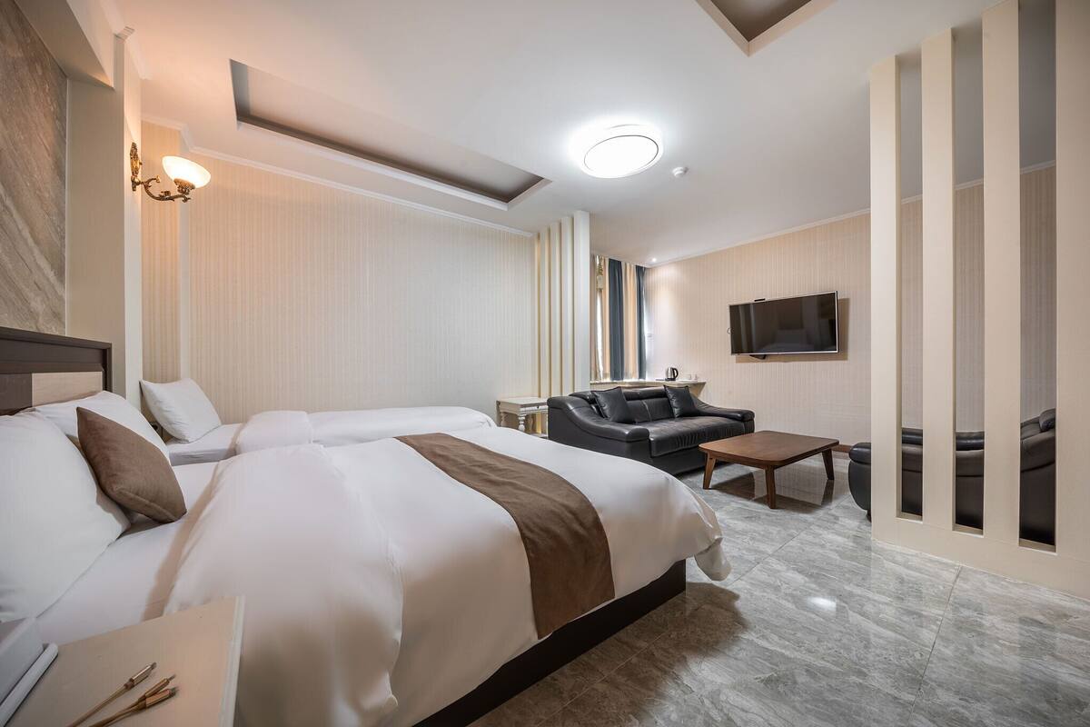 A hotel room with two beds, a sofa, a TV, and a small table.