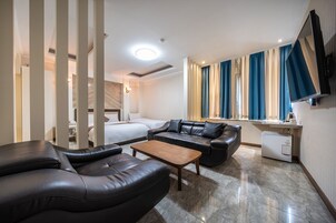 Una habitación de hotel moderna con sofá de cuero, una mesa de centro de madera, una cama y una pequeña cocina.