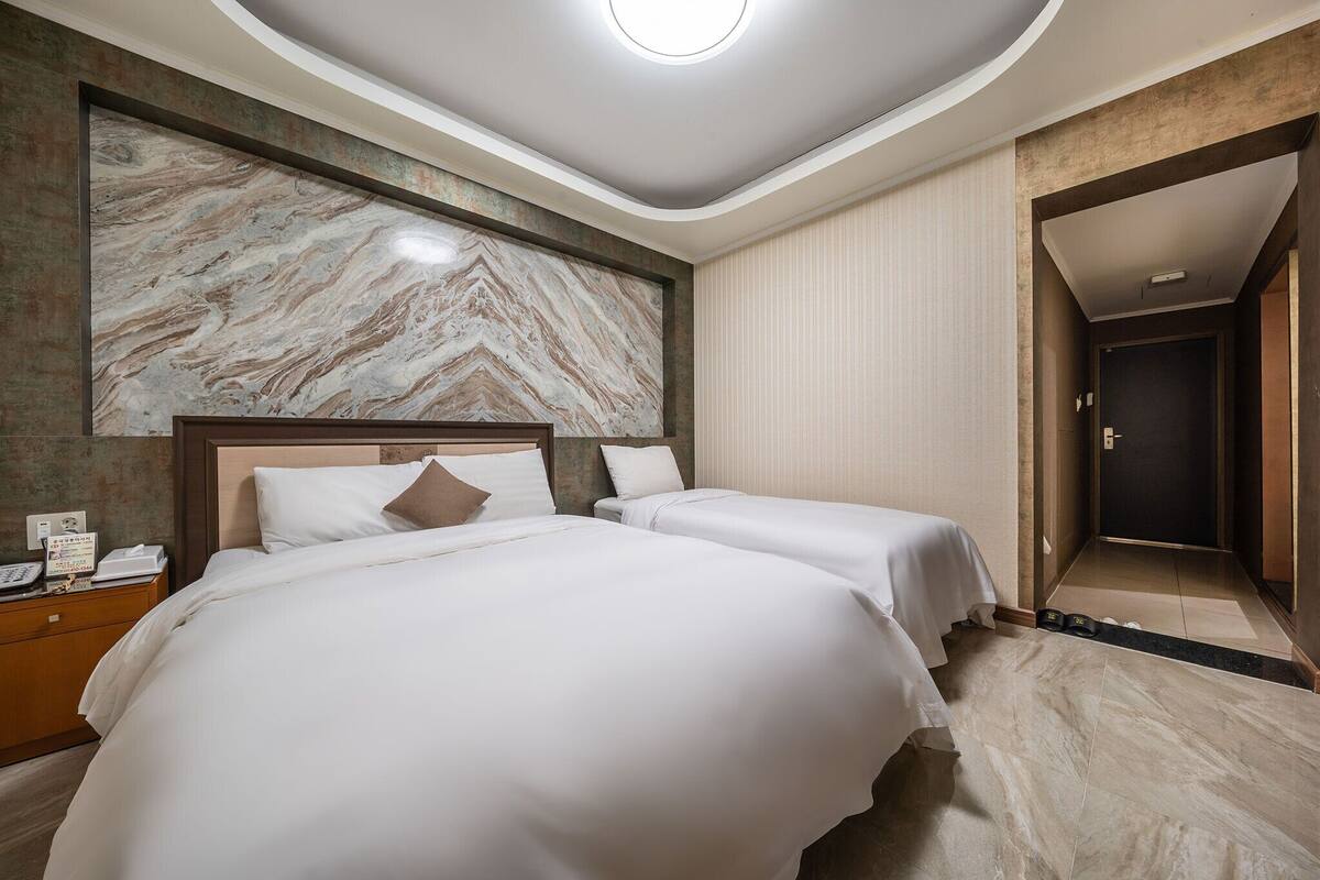 A hotel room with two beds, a marble wall, a wooden headboard, and a large mirror.